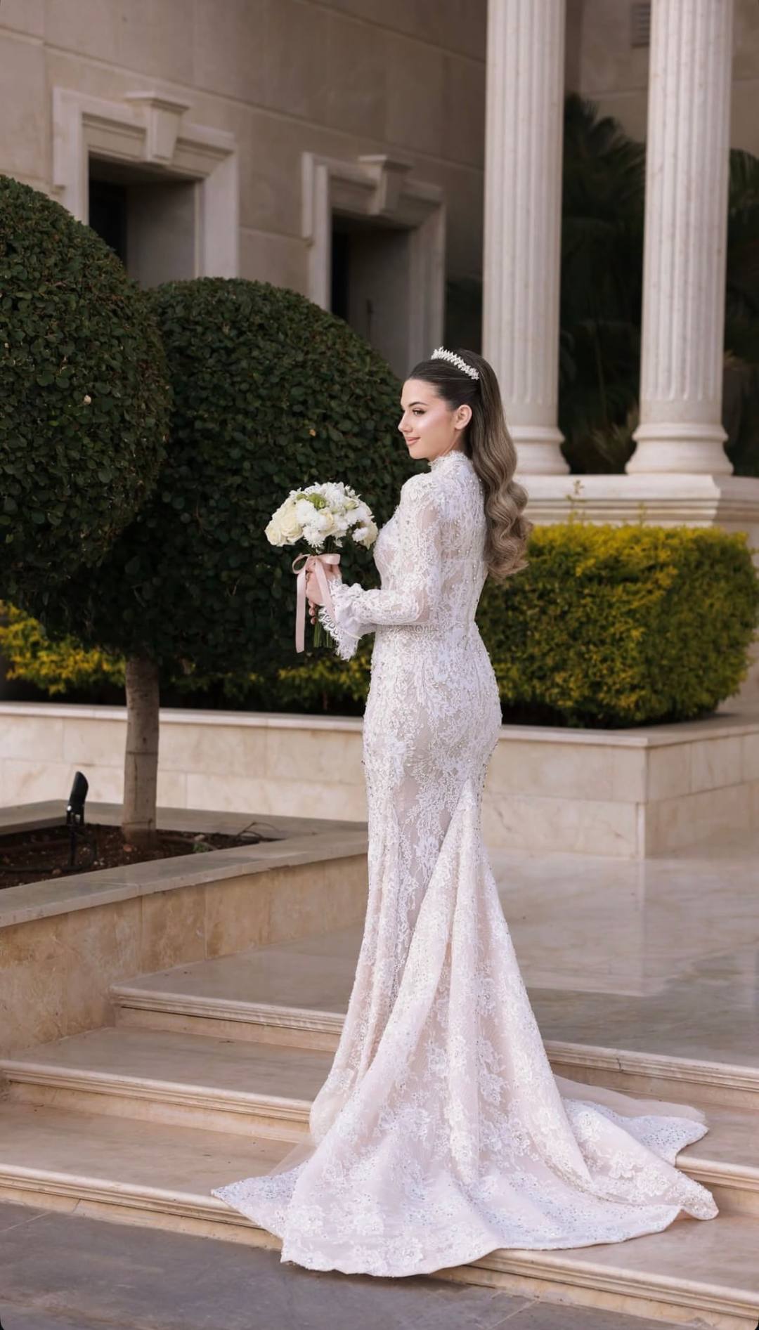 Bride in a lace gown holding a white bouquet on marble steps