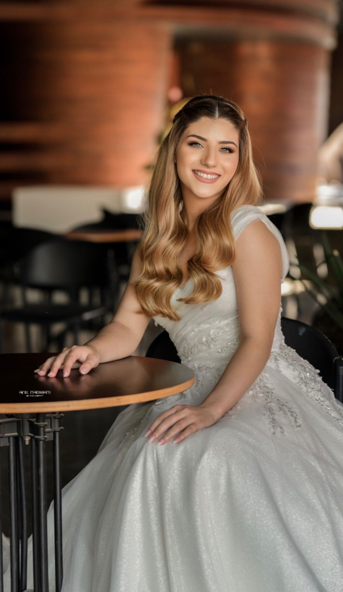 Smiling bride in a beaded gown seated at a café table