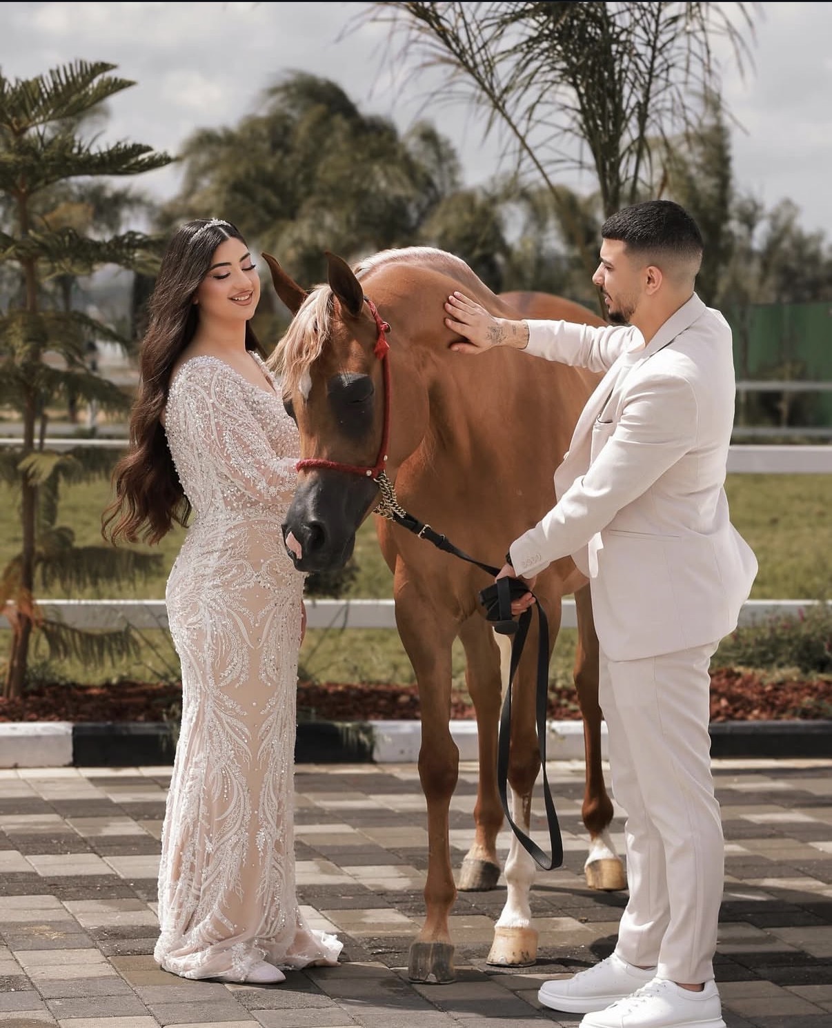 Bride and groom in a white suit beside a chestnut horse