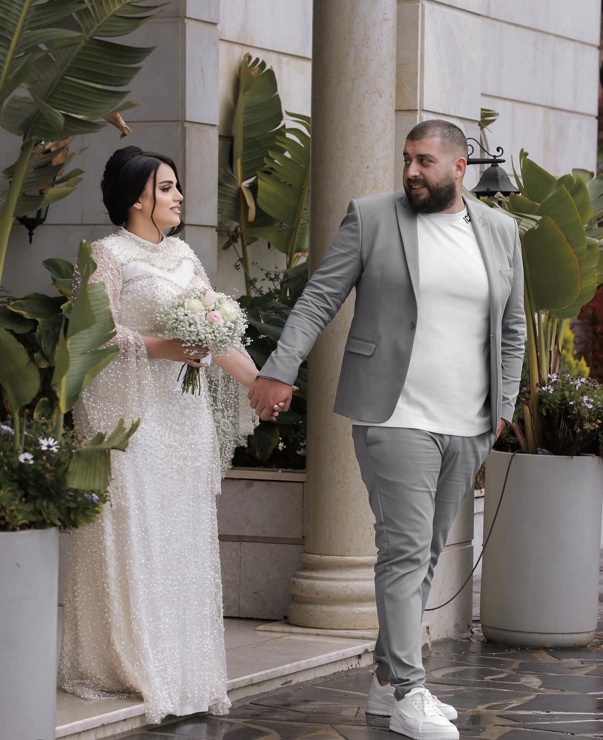 Bride with a bouquet walking with the groom past stone columns